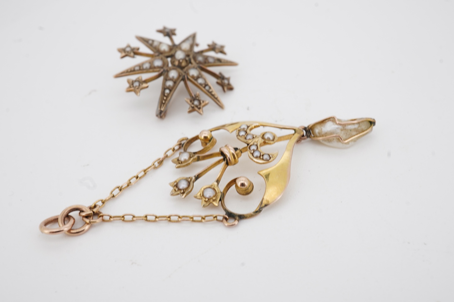 An Edwardian Art Nouveau 9ct, seed and baroque pearl set drop pendant, overall 55mm, together with an Edwardian style 9ct gold and seed pearl set starburst brooch.